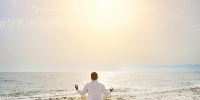 A man meditating on the beach facing a calm sea