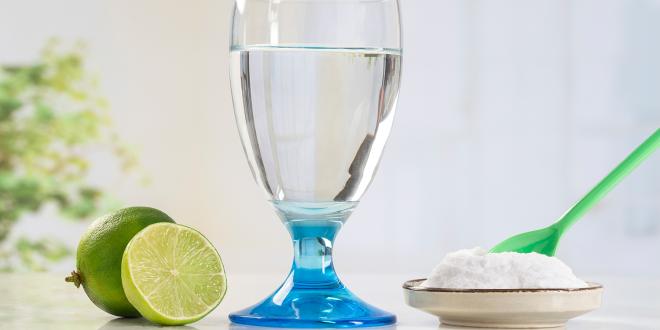 A glass of water, a sliced lime and a small dish of baking soda with a green spoon in it.