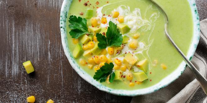 a bowl of creamy green soup with corn, diced avocado, and spices